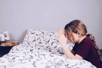 Teenage girl in pajamas on the bed. Pray on your knees with folded hands. Prayer.