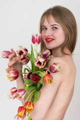 Portrait of gorgeous young lady feeling excited to receive bunch of tulips for Woman's Day and covering chest with flowers, looking at camera. Lovely blonde woman getting flowers for spring holiday