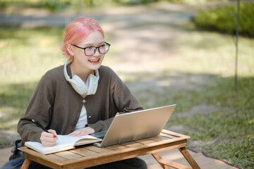 Young woman with a laptop and notes studying in the park for education in nature to relax and learn online.