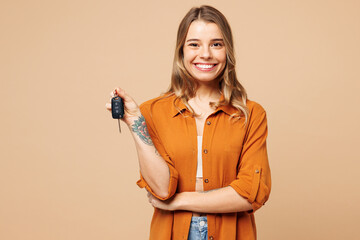Young smiling happy Caucasian woman she wears orange shirt casual clothes hold in hand car keys fob keyless system isolated on plain pastel light beige background studio portrait. Lifestyle concept.
