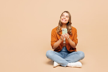 Full body young woman wear orange shirt casual clothes sits hold in hand use mobile cell phone look...