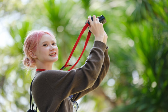 Beautiful Young artist Woman taking photo in flowers garden. Young cute girl carry the camera in the garden.