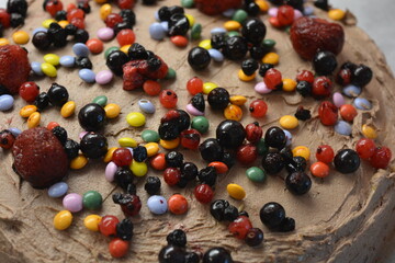 Bakery, homemade delicious pastries, sponge cake with brown cream sprinkled with bright colored candies with pieces of fruit.