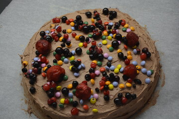 Bakery, homemade delicious pastries, sponge cake with brown cream sprinkled with bright colored candies with pieces of fruit.