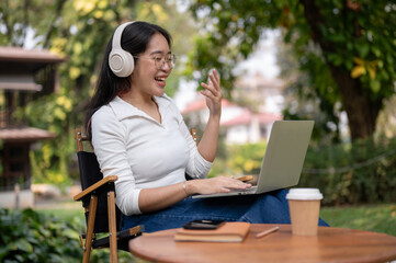 A happy Asian woman is having an online meeting, working outdoors at her backyard garden.