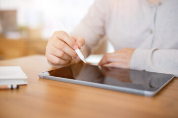 A cropped shot of a woman working on her digital tablet at a table indoors or in a minimalist cafe.