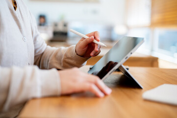 A side view image of a woman working remotely at a cafe, using her digital tablet.