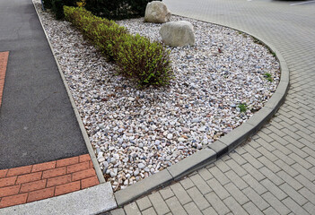 ornamental flower bed with perennial pine and gray granite boulders, mulched bark and pebbles in an urban setting near the parking lot shopping center. - obrazy, fototapety, plakaty