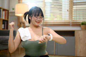 Cheerful Asian woman checking exercise results on smartwatch after workout