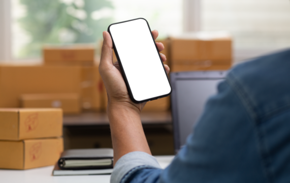 person holding smartphone with transparent screen at workplace with cartons parcel box background, design on smartphone , small business, online shopping , shipping , and delivery concept, png file