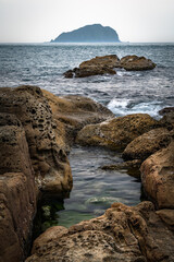 Beautiful rocks nearby the coastline, and Keelung island in the distance across the ocean in a cloudy day, shoot in long lens, in Keelung city, Taiwan.