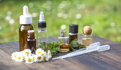 bottles of essential oil and daisies with fresh mint leaf on a wooden table  outdoors