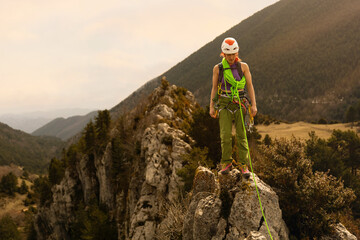 A woman is standing on a rock with a green rope. She is wearing a green outfit and a helmet. Concept of adventure and excitement, as the woman is preparing to climb the mountain