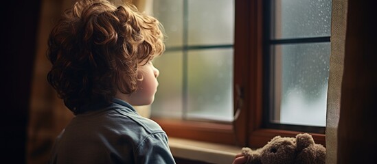 Boy observing rain from a window - obrazy, fototapety, plakaty