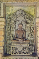 A finely detailed stone sculpture of a  Jain Tirthankara ADINATH,  with a serene expression, surrounded by ornate carvings 