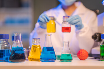 Close up female scientist in white lab coat working in biotechnological laboratory, using microscope, pipette, glass flask in clinical laboratory.