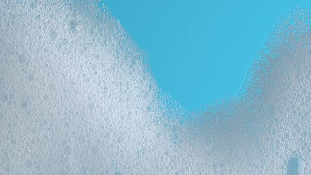 White soap suds flowing down window glass on blue background. Cleaning windows with cleaning disinfectant. Hygiene, disinfection, housework, household, cleanup, washing. Taking a shower