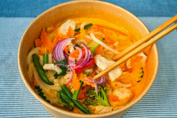 Red curry with vegetable, chicken meat and cocoa milk in bowl and chopsticks on blue. - 763864703