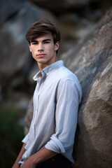 portrait of a handsome young man standing in front of a large rock