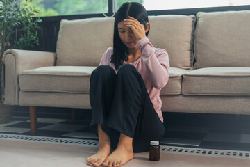 Depressed Asian woman sitting next to the sofa sad, feeling tired, lonely and unhappy.