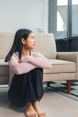 Depressed Asian woman sitting next to the sofa sad, feeling tired, lonely and unhappy.