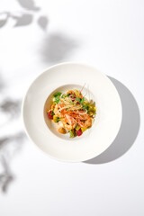 Elegant food - salad with shrimp and avocado on white table with harsh shadow. Flashy food concept. Seafood salad with shrimp, tomatoes and avocado on white plate with sunlight.