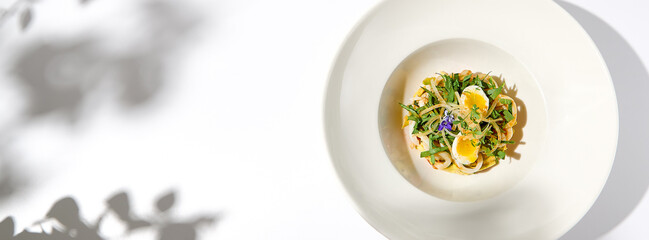 Healthy salad with squid and avocado on white plate with harsh shadows. Calamari salad with vegetables and eggs on white background with shadows of leaves. Summer food menu.