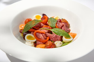Salad with roast beef, vegetables and eggs on white table with harsh shadows. Steak salad in modern style with shadows of leaves. Flashy food. Meat salad with pastrami in summer menu.