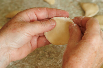 A close-up of an old woman's hands as she molds a vareniki mold out of dough. The process of making dough for varenyky by hand.