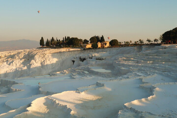 The travertines of Pamukkale early in the morning with hot air balloons rising in the back,...