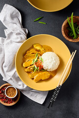 Curry chicken and rice served in a modern ceramic bowl, top view on a textured black background