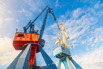 Two harbor cranes against a background of blue sky, bottom view.
