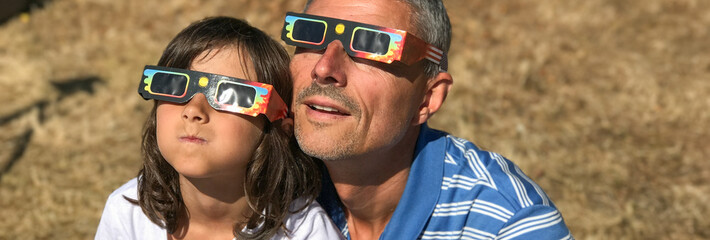 Fototapeta premium Father and daughter looking at the sun during a solar eclipse on a country park, family outdoor activity