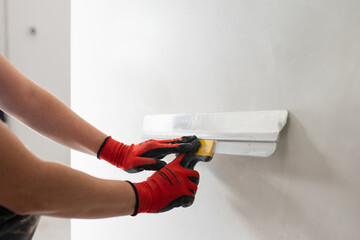 A professional builder levels the walls with putty - preparing the walls for painting and...