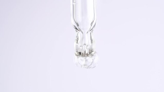 Macro shot of drop hanging down from chemical dropper. Cosmetics liquid serum dripping from laboratory glass pipette.