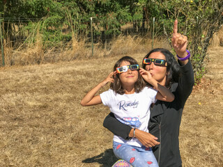 Mother and daughter looking at the sun during a solar eclipse on a country park, family outdoor...