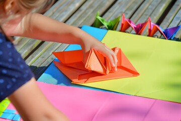 preschool kid folding bright origami paper on a mat - obrazy, fototapety, plakaty