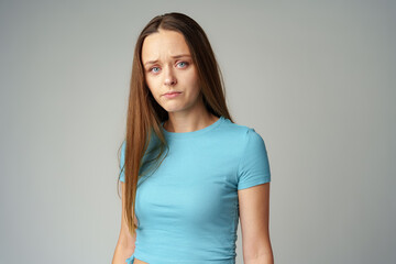 Obraz premium Portrait of sad displeased offended young woman in blue T-shirt on gray background