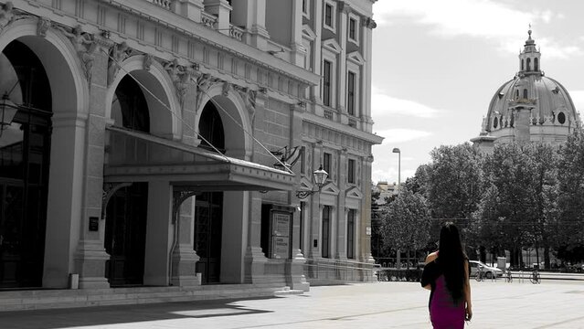 Woman in purple dress walking past historical buildings in black and white. Slow motion, wide shot. Karlskirche at backdrop, in Vienna.