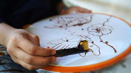 Batik making process, a handmade traditional art from Indonesia. Person carefully trace the butterfly motif on a traditional batik fabric. Produced by technique of wax-resist dyeing applied to fabric.