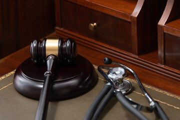 A close-up of a judge's gavel and a black stethoscope on top of a legal book, signifying the...