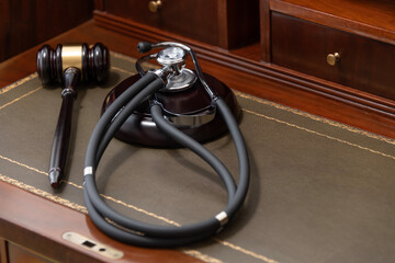 A close-up of a judge's gavel and a black stethoscope on top of a legal book, signifying the...