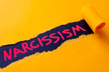 Black surface, with word Narcissism, in red. Underneath torn yellow cardboard.
