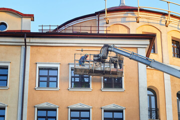 Workers using  cradle crane to install an advertisement board on building facade. Men on crane installing outdoor advertising  at height. Man work on aerial platform