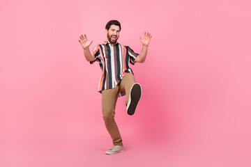 Fototapeta na wymiar Full body photo of energetic young man in striped shirt steps towards you showing his new sneakers sole isolated on pink color background