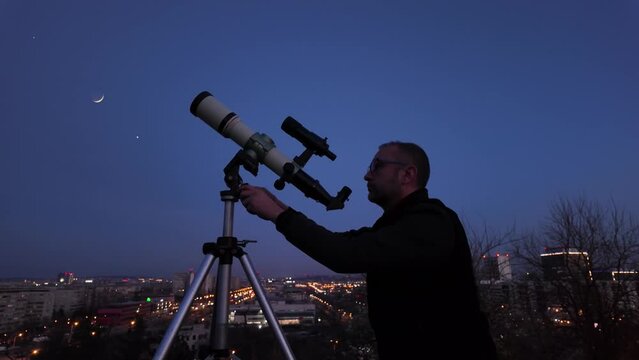 Amateur astronomer looking at the evening skies, observing planets, stars, Moon and other celestial objects with a telescope in urban city area.	
