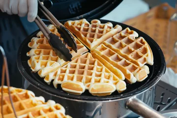 Fototapeten person taking waffles out of iron with tongs © altitudevisual