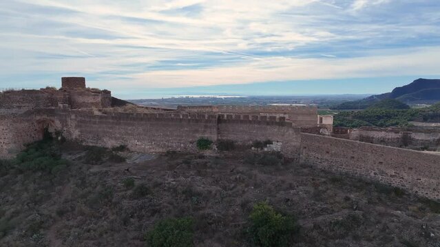 drone flight with high quality footage visualizing the fortress on the hill with its imposing walls and a background of mountains with a blue sky with white clouds in winter in Valencia Spain