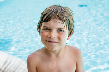 Portrait of happy little kid boy resting near the pool and having fun on family vacations in a hotel resort. Healthy child playing in water, swimming and splashing.