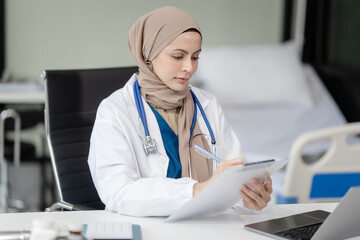 Portrait of Muslim middle age female doctor with head scarf in white lab coat and stethoscope while consult online in laptop. advice on good mental health management and medical treatment costs.